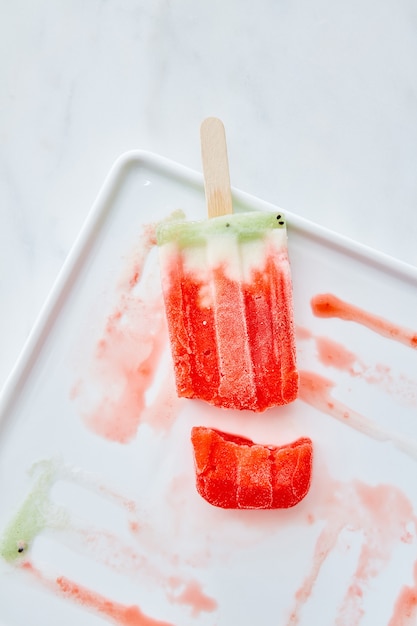 Foto sorvete de frutas derretendo em um palito com respingos em um prato