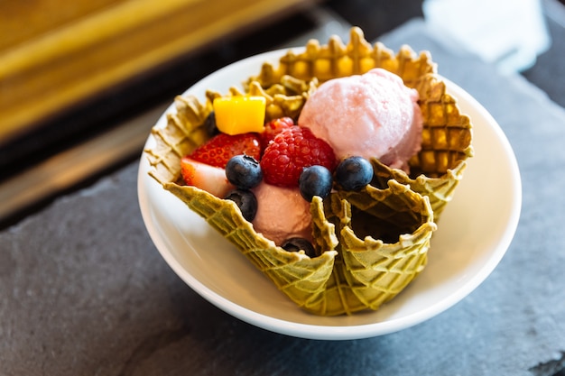 Foto sorvete de morango com frutas frescas dentro da tigela de waffle fina crocante.