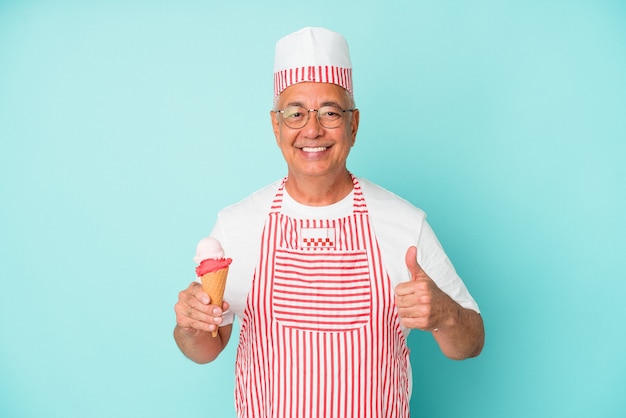 Sorveteira sênior americana segurando um sorvete isolado em um fundo azul, sorrindo e levantando o polegar