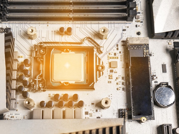 Sostenga el asa de la CPU e insértela en la ranura de la CPU en la placa base. Es una placa base vieja con mucho polvo. Ponga una luz naranja en la ranura de la CPU. Hay una ranura de RAM al lado. Hay un condensador.