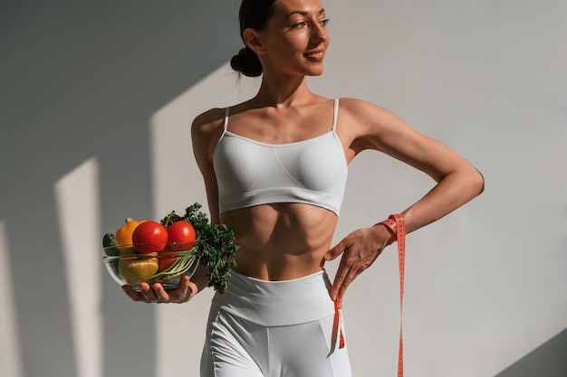 Foto sosteniendo alimentos saludables mujer caucásica joven con forma de cuerpo delgado está adentro en el estudio