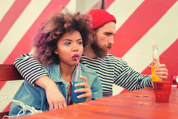 Sosteniendo bebidas. Jóvenes pensativos que parecen somnolientos mientras están sentados a la mesa y beben alcohol por la mañana