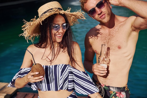 Sosteniendo bebidas en las manos Alegre pareja o amigos juntos en la piscina en vacaciones