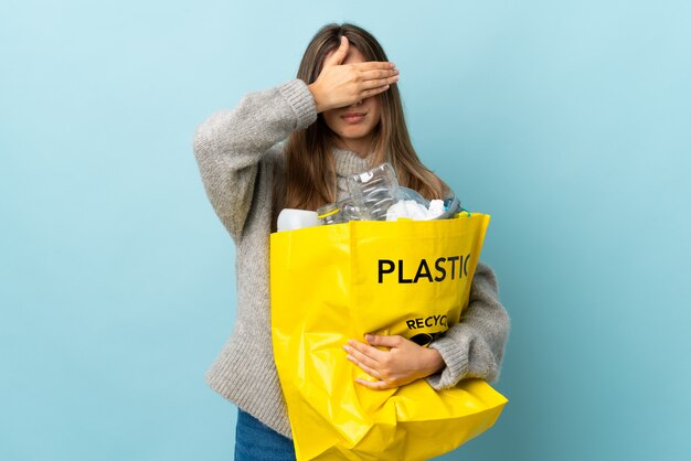 Sosteniendo una bolsa llena de botellas de plástico para reciclar sobre ojos azules que cubren con las manos