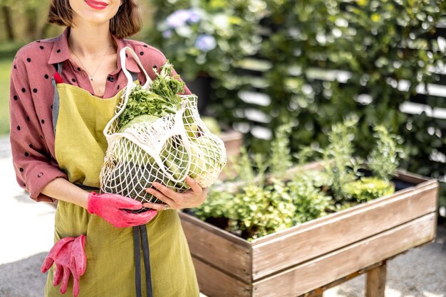 Sosteniendo una bolsa de malla llena de verduras frescas y verduras en el jardín de su casa