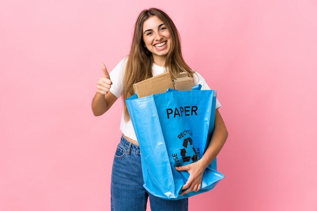 Sosteniendo una bolsa de reciclaje llena de papel para reciclar sobre rosa aislado dando un gesto de aprobación
