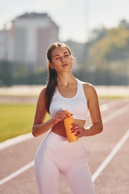 Sosteniendo una botella de agua Mujer joven en ropa deportiva está haciendo ejercicio al aire libre