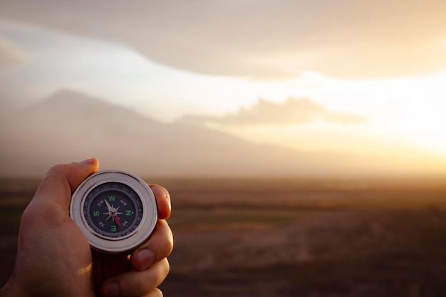 Sosteniendo una brújula contra el telón de fondo de una montaña al atardecer