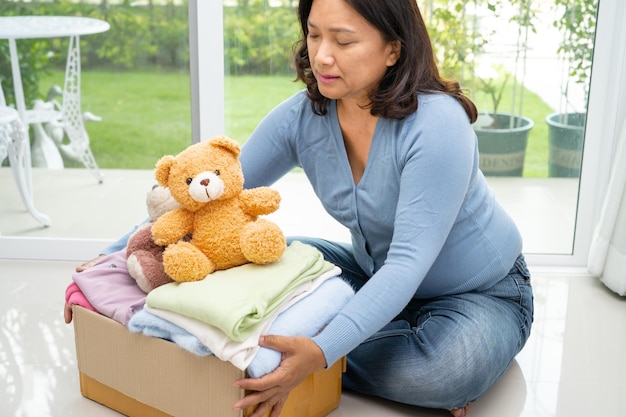 Sosteniendo una caja de donación de ropa con ropa usada y muñecas en casa para ayudar a los pobres del mundo