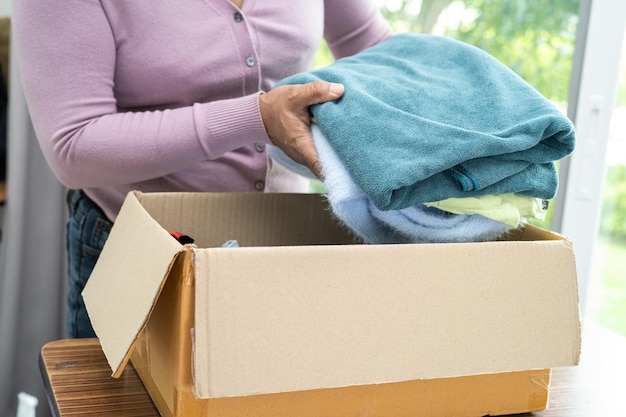 Sosteniendo una caja de donación de ropa con ropa usada y muñecas en casa para ayudar a los pobres del mundo