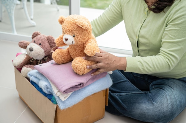 Sosteniendo una caja de donación de ropa con ropa usada y muñecas en casa para ayudar a los pobres del mundo