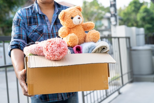 Sosteniendo una caja de donación de ropa con ropa usada y muñecas en casa para ayudar a los pobres del mundo