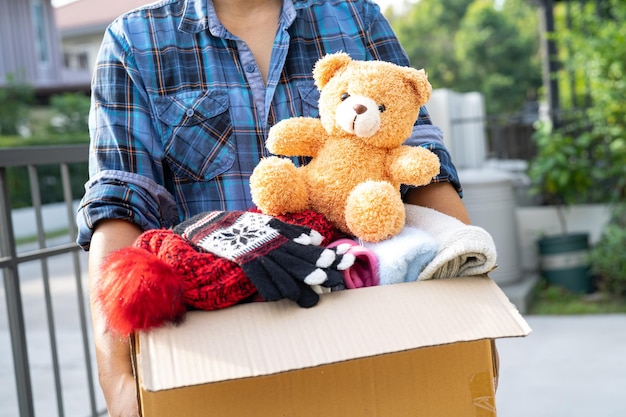 Sosteniendo una caja de donación de ropa con ropa usada y muñecas en casa para ayudar a los pobres del mundo
