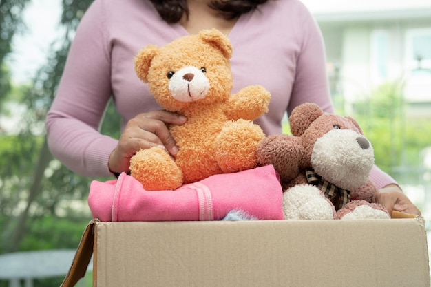 Sosteniendo una caja de donación de ropa con ropa usada y muñecas en casa para ayudar a los pobres del mundo