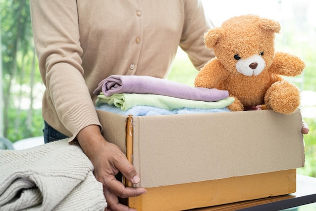 Sosteniendo una caja de donación de ropa con ropa usada y muñecas en casa para ayudar a los pobres del mundo