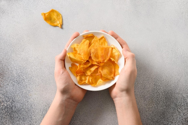 Sosteniendo chips de frutas yaca en plato blanco