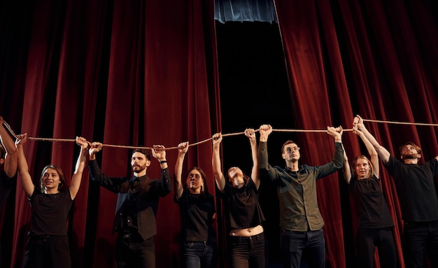 Foto sosteniendo la cuerda en las manos por encima de la cabeza grupo de actores en ropa de color oscuro en el ensayo en el teatro