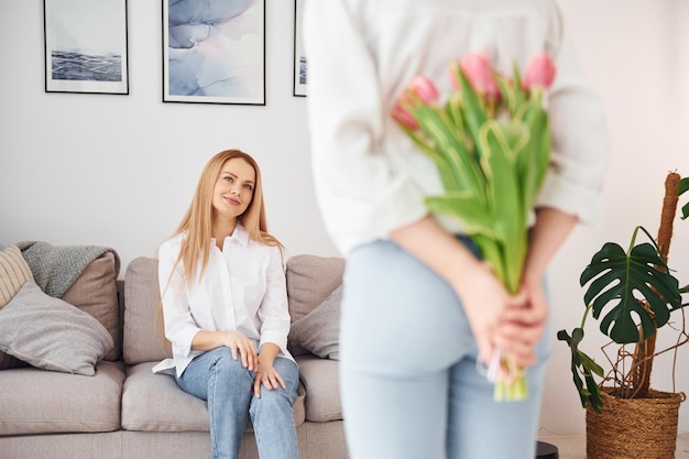 Sosteniendo flores La joven madre con su hija está en casa durante el día