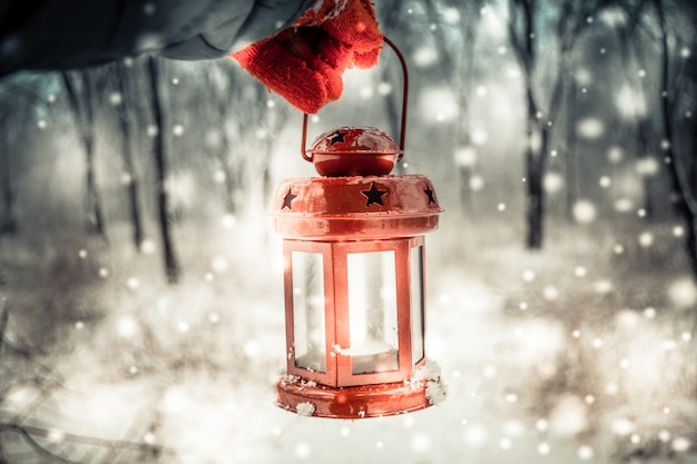 Sosteniendo una linterna de vela roja en el bosque de invierno
