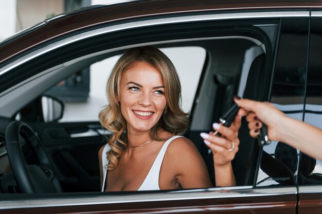 Sosteniendo las llaves del auto La mujer con ropa formal está adentro en el autosalon