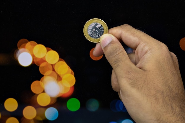 Sosteniendo una moneda de dinero brasileño en un fondo de luces borrosas