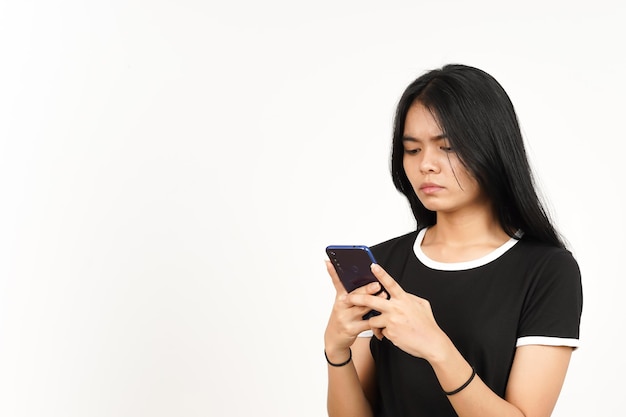 Sosteniendo o usando un teléfono inteligente con cara triste o enojada de una hermosa mujer asiática aislada en blanco
