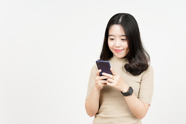 Sosteniendo o usando el teléfono inteligente y la sonrisa de una hermosa mujer asiática aislada en el fondo blanco