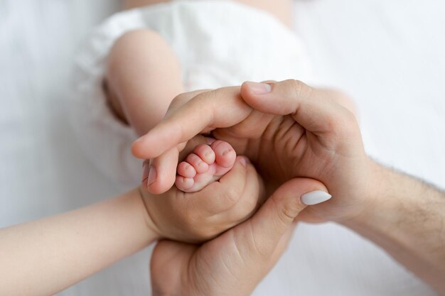 Sosteniendo los pies del bebé en las manos. Idea de sesión de fotos familiar. Pies de bebé recién nacido sobre fondo blanco.