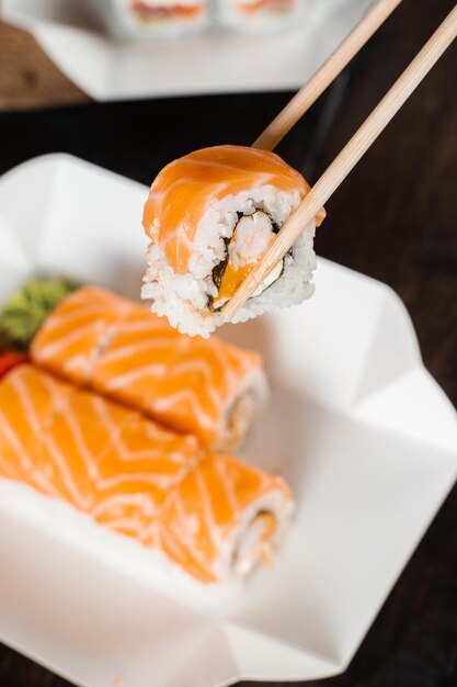 Sosteniendo un rollo de Filadelfia con palillos para sushi. Roll con salmón, camarones y mango. Entrega de comida japonesa.