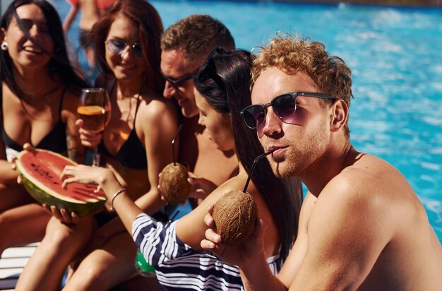 Sosteniendo sandía Grupo de jóvenes felices divertirse en la piscina durante el día