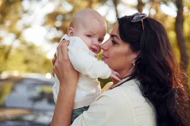 Foto sosteniendo a su bebé en las manos una hermosa madre con su pequeño hijo está al aire libre en el bosque