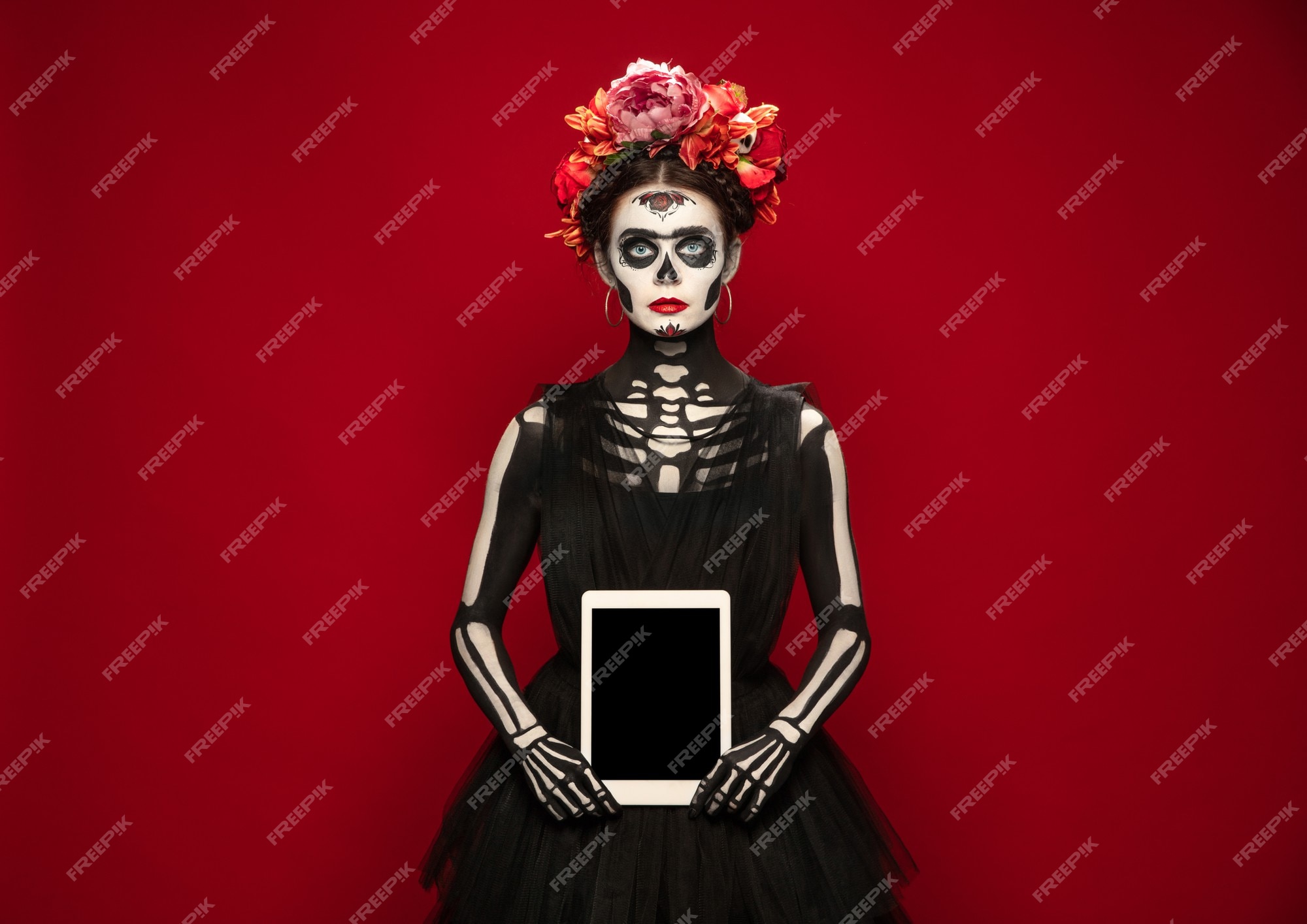 Sosteniendo la tableta. chica joven como santa muerte santa muerte o  calavera de azúcar con maquillaje brillante. retrato aislado sobre fondo  rojo de estudio. celebrando halloween o día de muertos. copyspace en