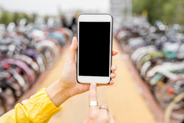 Sosteniendo un teléfono inteligente con pantalla vacía para copiar y pegar en el fondo del estacionamiento de bicicletas