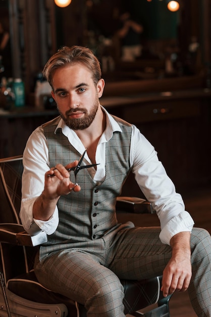 Sosteniendo las tijeras El guapo barbero está en el salón