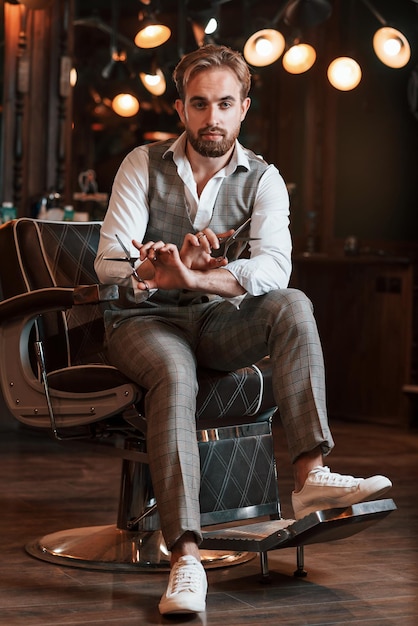 Sosteniendo las tijeras El guapo barbero está en el salón