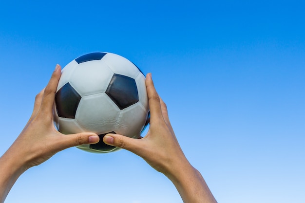 sostiene un balón de fútbol en el cielo sobre fondo de cielo azul.