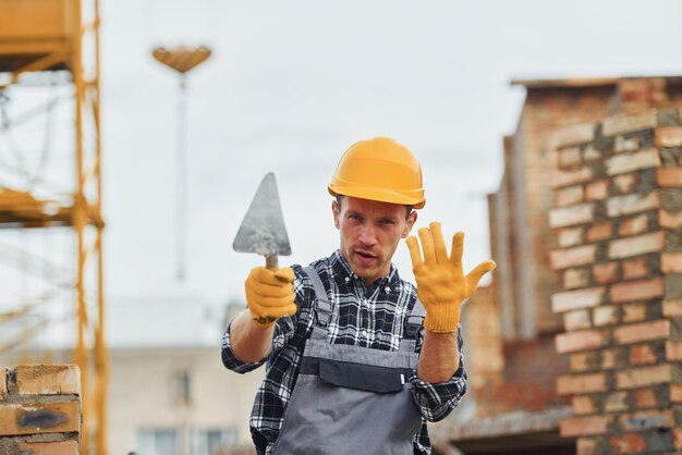 Sostiene espátula Trabajador de la construcción en uniforme y equipo de seguridad tiene trabajo en la construcción