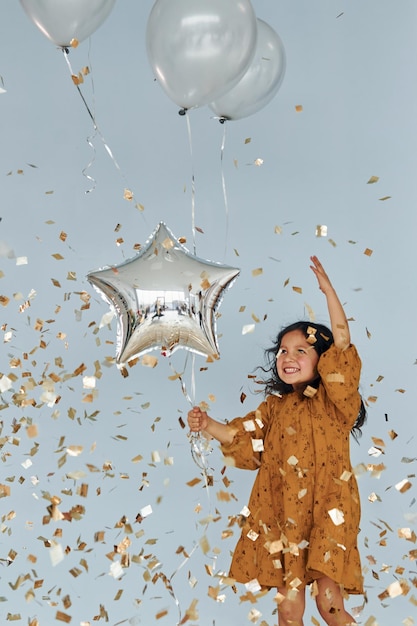 Sostiene globos Niña feliz de pie y diviértete en el interior de la fiesta de cumpleaños