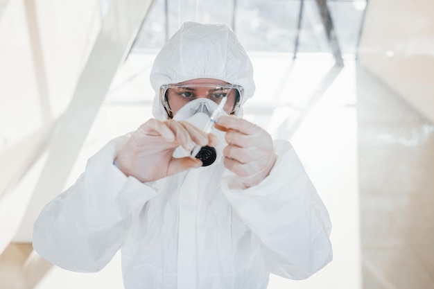 Foto sostiene una jeringa con medicina doctora científica en bata de laboratorio, anteojos defensivos y máscara de pie en el interior