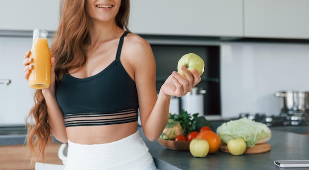 Sostiene la manzana en la mano La joven europea está en el interior de la cocina con comida saludable