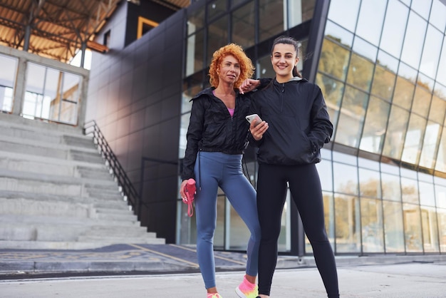 Foto sostiene el teléfono en las manos dos amigas con cuerpos deportivos tienen un día de fitness al aire libre