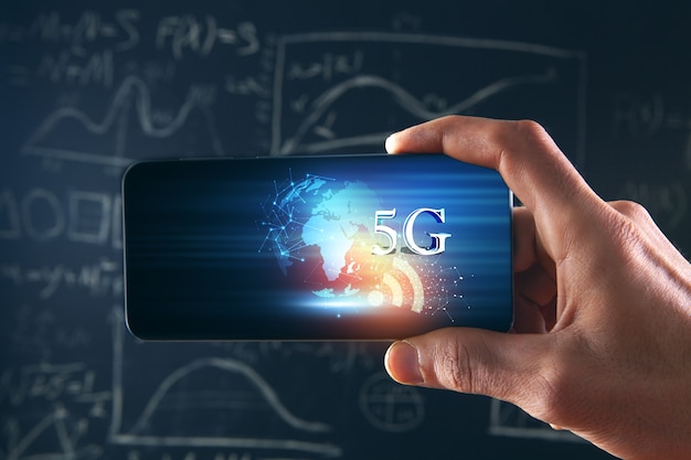 Sostiene un teléfono con un planeta y 5G sobre un fondo de pizarra