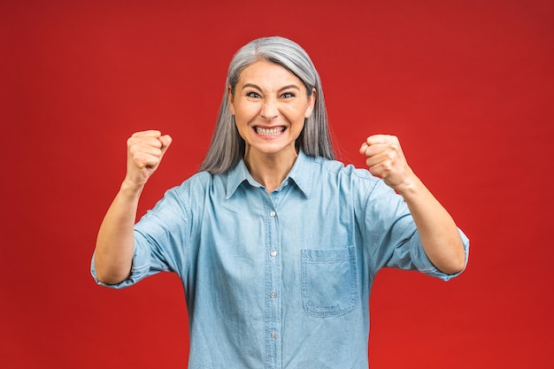 Sou vencedor Retrato de uma mulher madura sênior feliz e alegre gesticulando vitória isolada sobre fundo vermelho