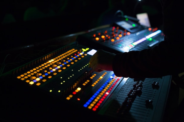 Soundman trabajando en la mesa de mezclas. Manos en los controles deslizantes.