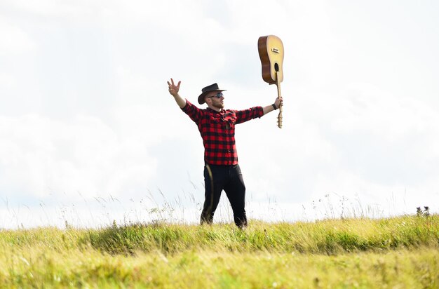 Sounds like music western camping e caminhadas moda hipster feliz e livre homem sexy com violão em camisa quadriculada cowboy homem com violão tocador de música country