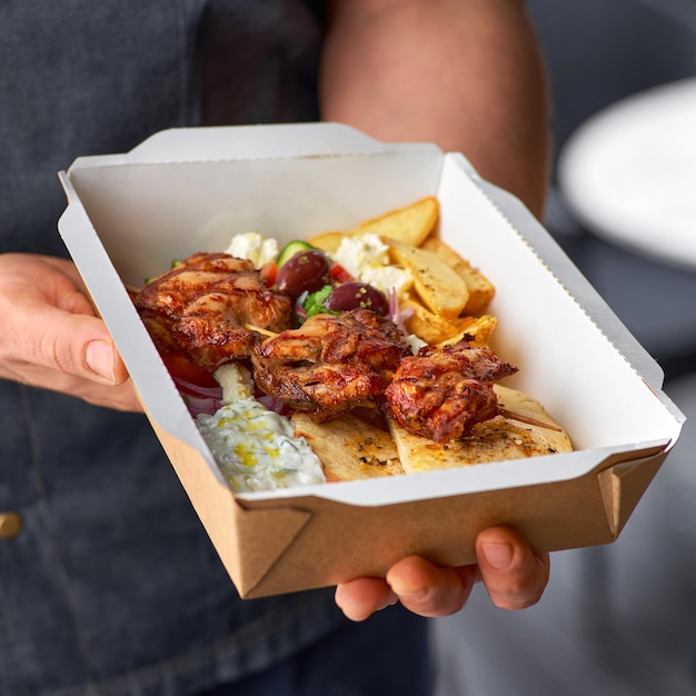 Foto souvlakisalad grego e giroscópios tiram menu servindo em recipiente de papel reciclável nas mãos do chef