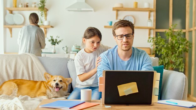 Soziale Distanzierung. Ein vielbeschäftigter Vater versucht, zu Hause mit seinem Kind und seiner Frau zu arbeiten.