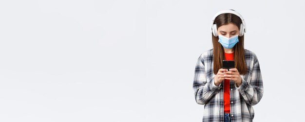 Soziale Distanzierung Freizeit und Lebensstil auf covid19 Ausbruch Coronavirus Konzept Süße Studentin Teenager-Mädchen in Kopfhörern, die Lieder in der Handy-Download-Musik-App auf weißem Hintergrund auswählen