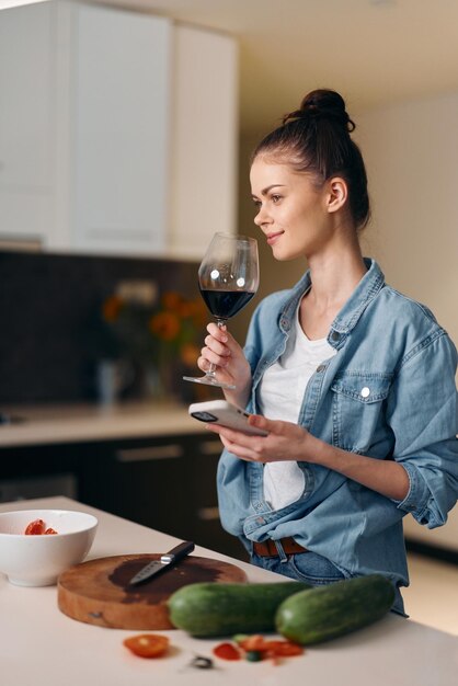 Sozinha na cozinha, uma jovem elegante a desfrutar de um copo de vinho vermelho em casa.