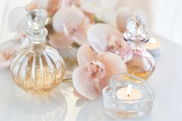 Foto spa bodegón con perfume y aceites aromáticos en botellas rodeadas de flores y velas.